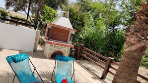 Two blue folding chairs with red flowers on a tiled patio, a brick oven, and a wooden fence. - Lovely 1-bed Palm Garden House in Perivolialarnaka (Pervolia)