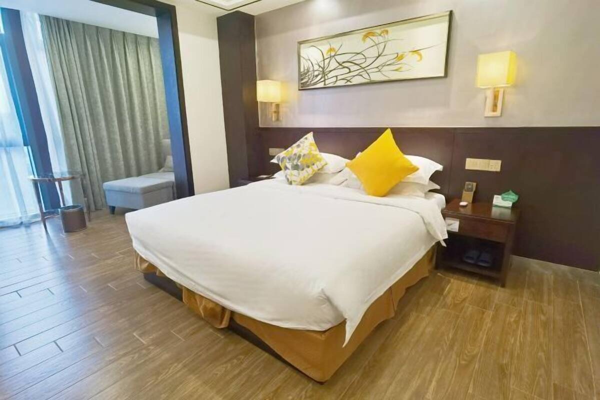 Quarto de hotel com uma cama grande, mesa de cabeceira, luminária e um quadro na parede.