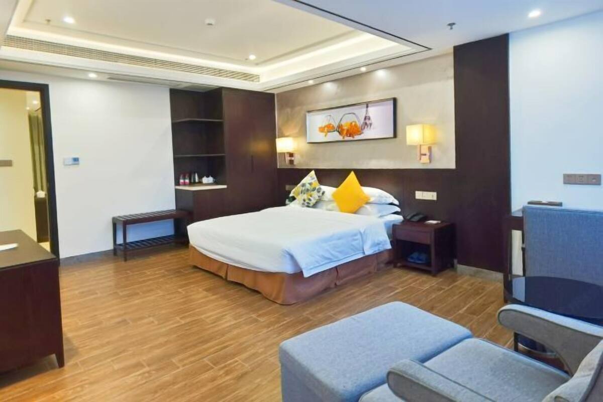 Quarto de hotel com uma cama grande, mesas de cabeceira, escrivaninha, cadeira e prateleira na parede com artigos de higiene pessoal.