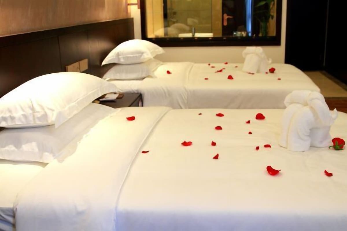 Two beds with white linens and pillows, each adorned with red rose petals and a white towel.