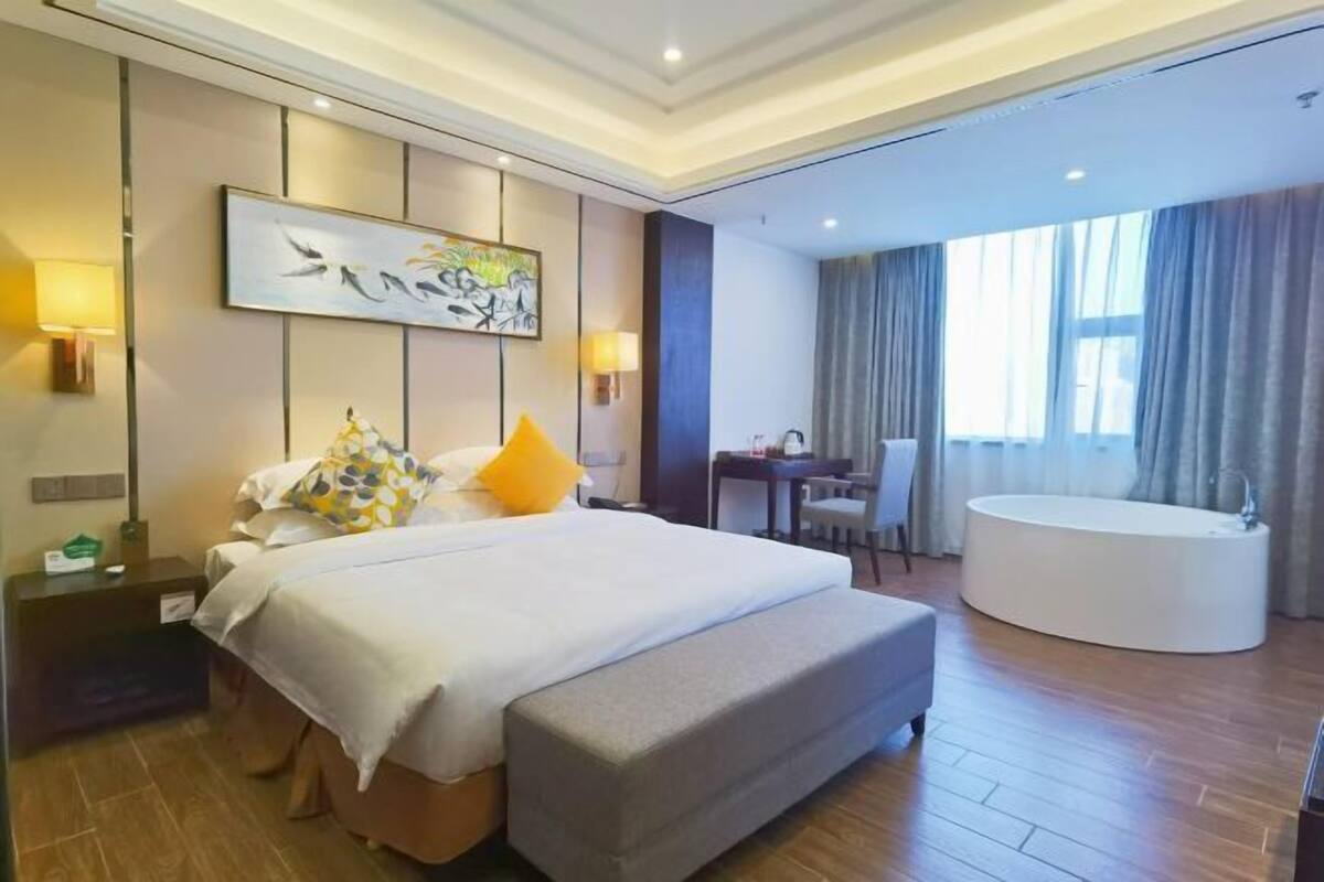 Quarto de hotel com cama grande, escrivaninha, cadeira e banheira.