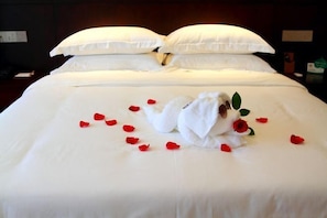 A neatly made bed with white linens, a swan-shaped pillow, and scattered rose petals. - Guangling Nanfan Hotel (Lingshui)
