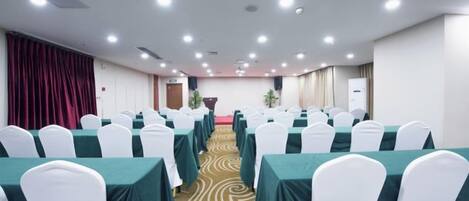 A conference room with rows of tables and chairs, a carpeted floor, and a stage at the front.