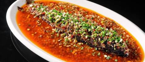 A white oval dish containing a whole fish in a red sauce, garnished with green herbs.
