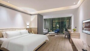 A modern hotel room with a large bed, a desk, and a seating area with a view of greenery through a glass wall. - Aixi Jialin Hotel(Chongqing Bishan Junhao Central Street Store) (Chongqing)