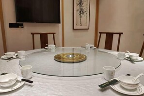 A round glass table with white plates, cups, and a tea set, surrounded by chairs in a room with a flat-screen TV and a framed artwork on the wall. - Aixi Jialin Hotel(Chongqing Bishan Junhao Central Street Store) (Chongqing)