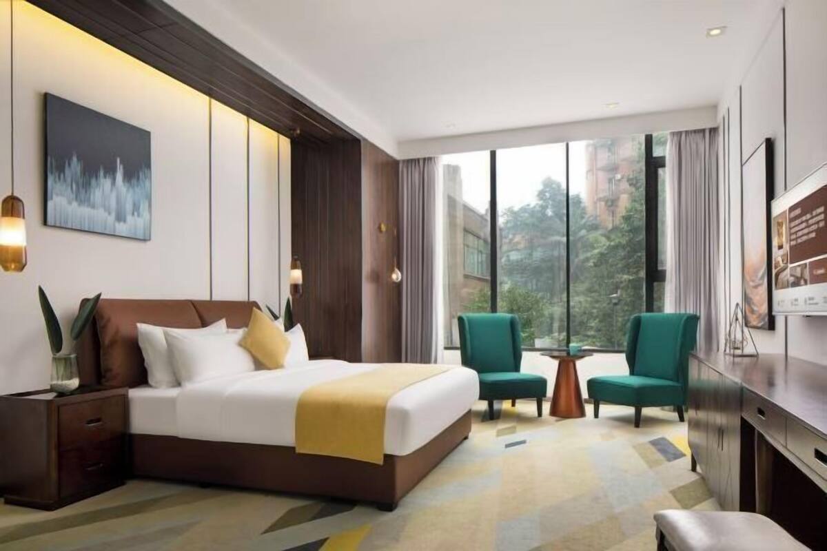 Ein modernes Hotelzimmer mit einem großen Bett, zwei Sesseln, einem kleinen Tisch und einem Fernseher.