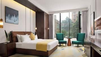 A modern hotel room with a large bed, two armchairs, a small table, and a TV.