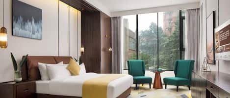 A modern hotel room with a large bed, two armchairs, a small table, and a TV.
