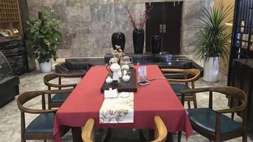 Un comedor con mantel rojo, sillas de madera y una mesa negra. Hay plantas en macetas y un jarrón con flores sobre la mesa.