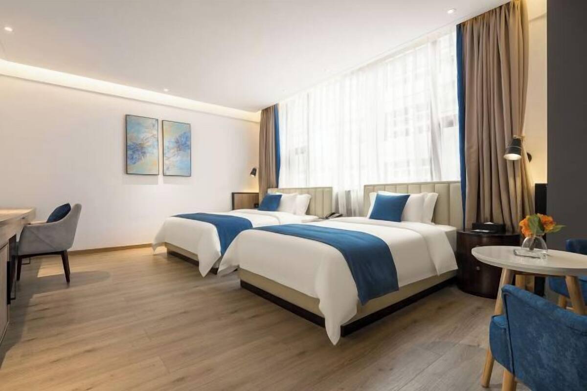 Ein modernes Hotelzimmer mit zwei Betten, einem Schreibtisch und einem kleinen runden Tisch.