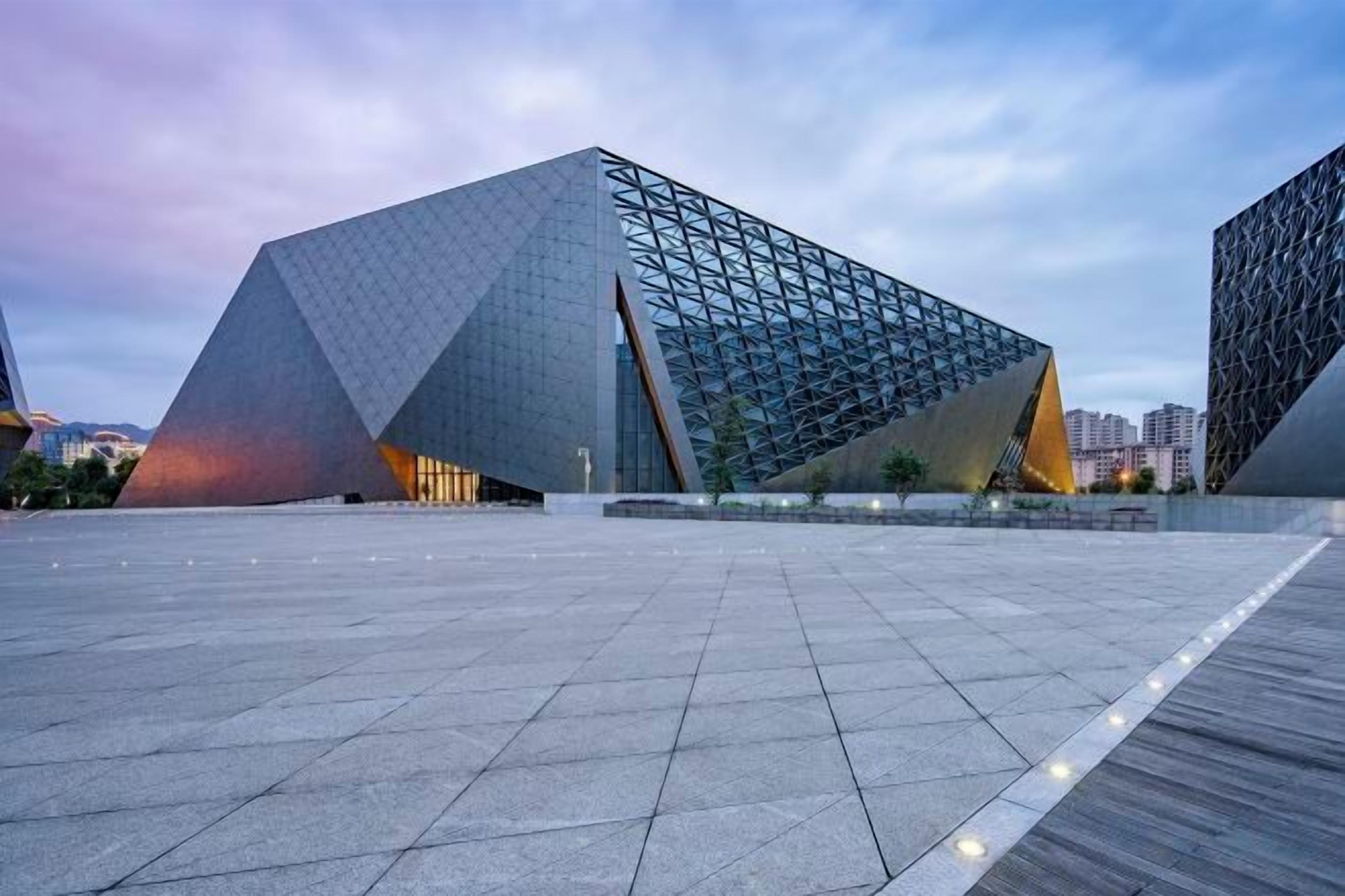 A modern architectural building with a geometric design, featuring a large open plaza in front.