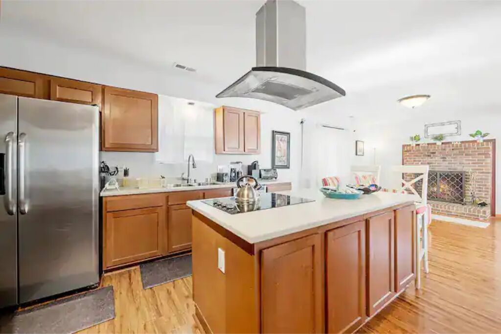 A modern kitchen with wooden cabinets, a stainless steel refrigerator, and a central island with a kettle.