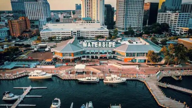 Un hôtel situé au bord de l’eau, reconnaissable à son grand panneau « WATERSIDE », avec des bateaux amarrés et une vue sur les gratte-ciel de la ville en arrière-plan.