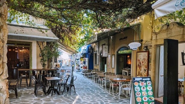 Une rue pavée avec des tables en terrasse, un panneau affichant le menu et un bâtiment sur lequel on peut lire l’inscription « Café ».