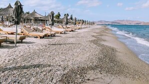 Une plage bordée de rangées de transats et de parasols, une plage de galets et une mer calme.