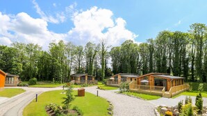 A lodge with wooden cabins, a covered deck, and a gravel driveway surrounded by trees. - Robin Lodge (Skipton)
