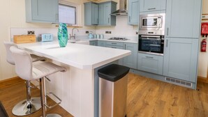 A modern kitchen with light blue cabinets, a white island with bar stools, stainless steel appliances, and a skylight. - Robin Lodge (Skipton)