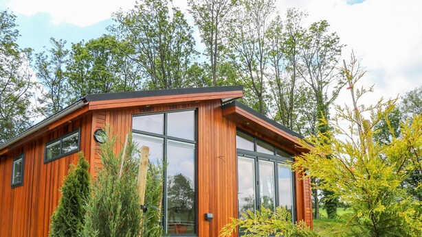 A modern wooden cabin with large windows, surrounded by rocks and greenery. - Robin Lodge (Skipton)