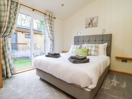A bedroom with a large bed, a grey headboard, and a view of a wooden deck through a sliding glass door.