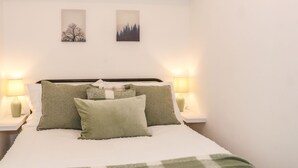 A neatly made bed with green and white bedding, two wall-mounted paintings, and bedside lamps on either side. - Hope Cottage (Thornton-Cleveleys)