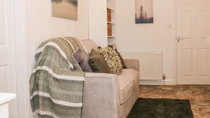 A cozy living room with a sofa covered in a striped blanket, a decorative deer head, and a framed forest scene on the wall. - Hope Cottage (Thornton-Cleveleys)