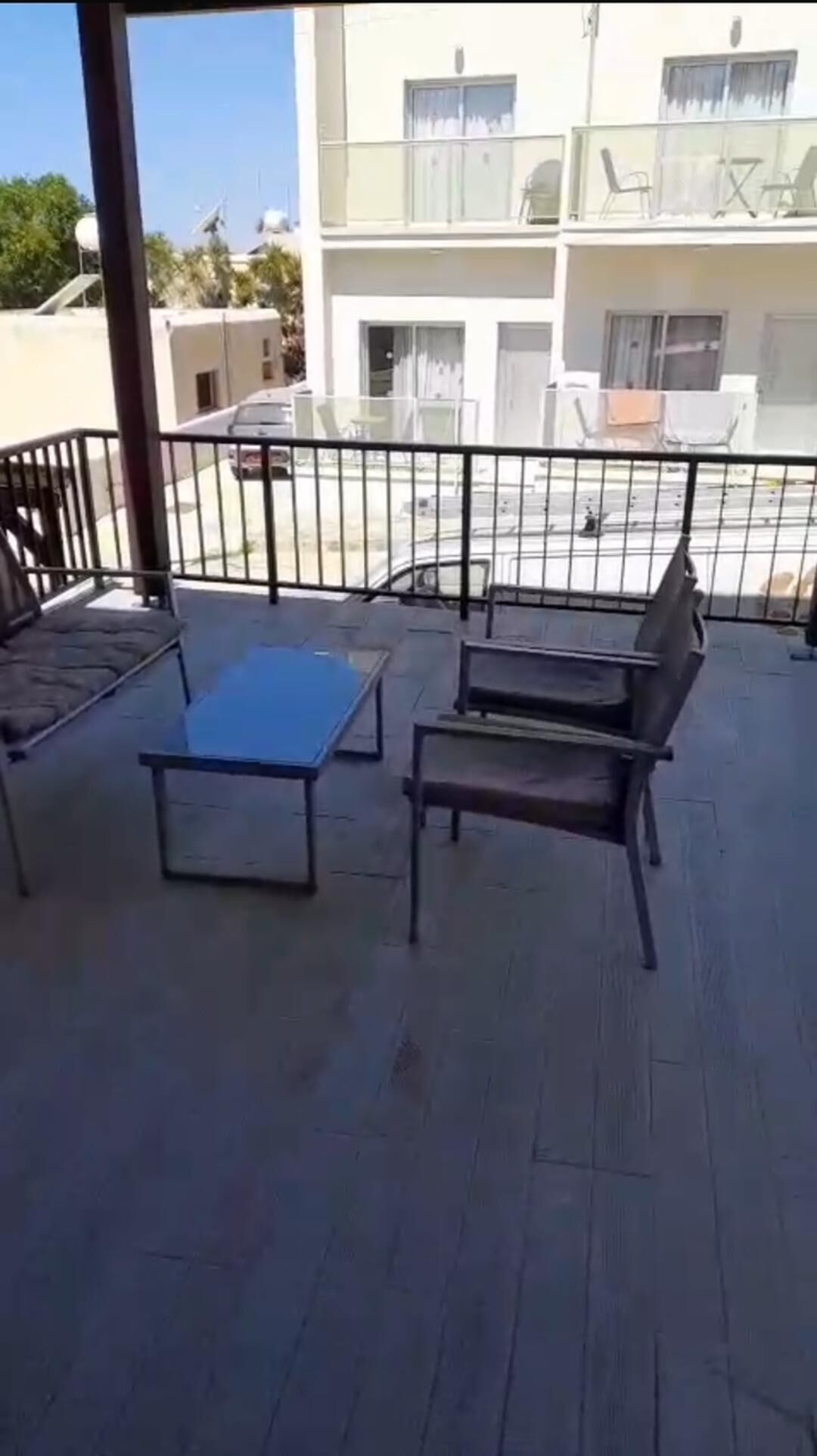 A balcony with a table and two chairs, a railing, and a building in the background.