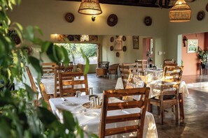 A dining area with wooden chairs and tables, hanging light fixtures, and wall decorations. - The Nkhosi Livingstone Lodge and Spa (Livingstone)
