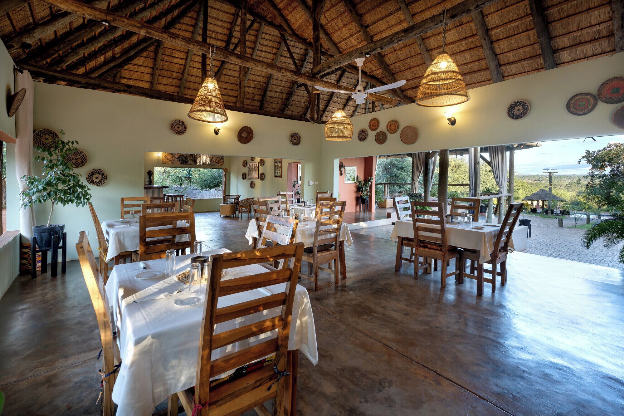 A restaurant with wooden tables and chairs, hanging lights, and a thatched roof.