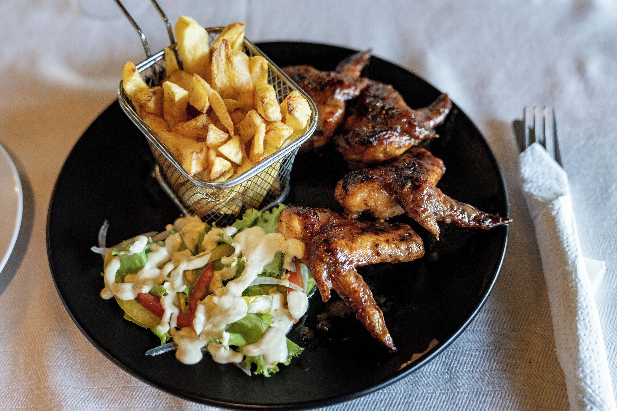 A plate with grilled chicken wings, a side of French fries, and a coleslaw salad.