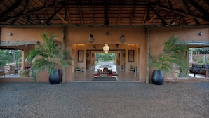 A covered outdoor area with a thatched roof, potted plants, and a central pathway leading to a door. - The Nkhosi Livingstone Lodge and Spa (Livingstone)