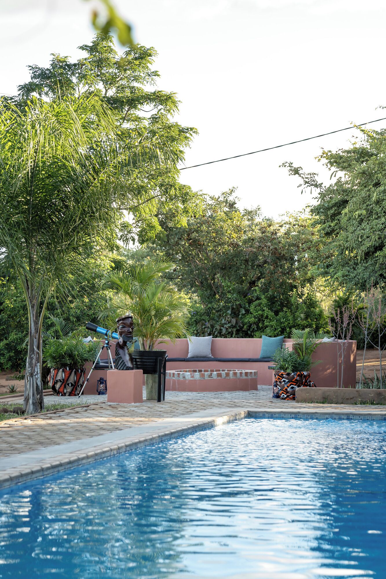 A swimming pool with a surrounding garden, a telescope, and a bench.