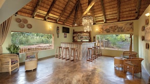 A spacious room with a high ceiling, a bar area, wicker furniture, and large windows offering a view of the outdoors. - The Nkhosi Livingstone Lodge and Spa (Livingstone)