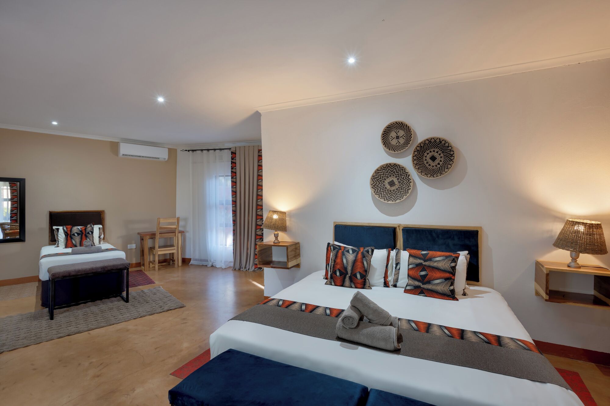 A hotel room with a bed, bedside tables, a desk, a chair, and a window with curtains.