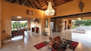 A spacious room with a high ceiling, a chandelier, a wooden floor, a large rug, and a sculpture of a hippo. - The Nkhosi Livingstone Lodge and Spa (Livingstone)