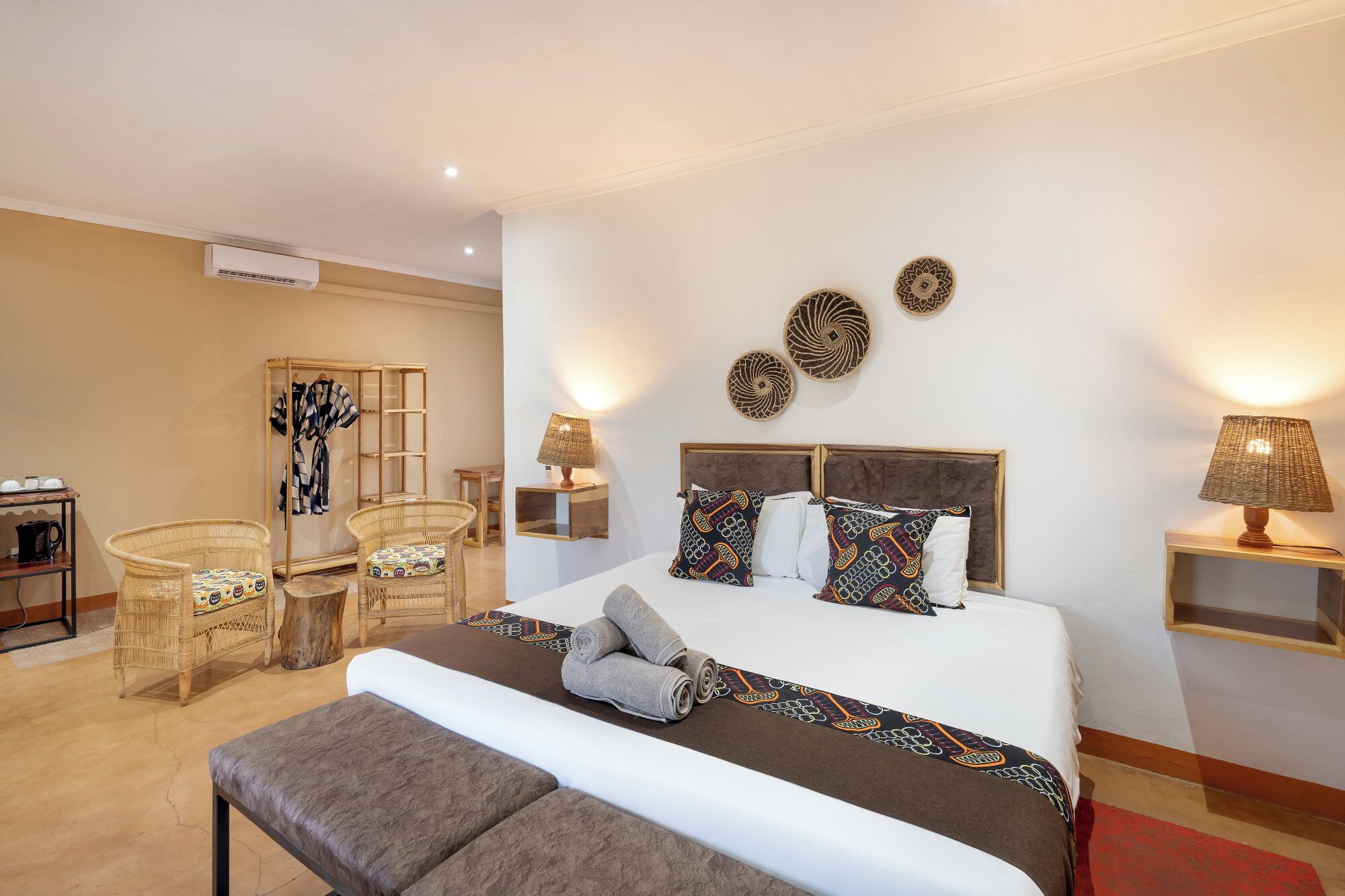A hotel room with a bed, two bedside tables, a chair, a small table, and a wardrobe.