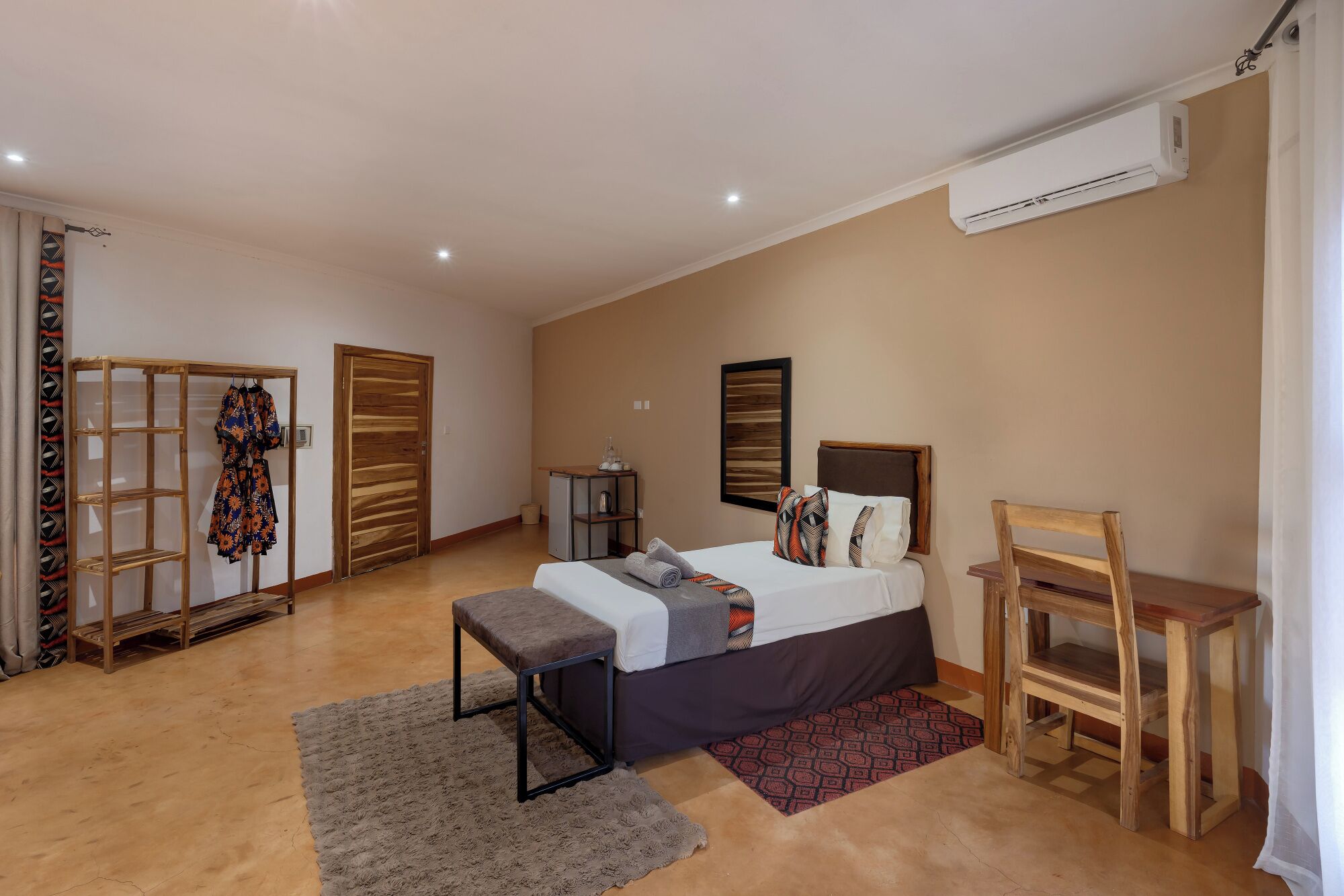 A bedroom with a bed, a wooden chair, a small table, a bench, an air conditioning unit, and a wardrobe.