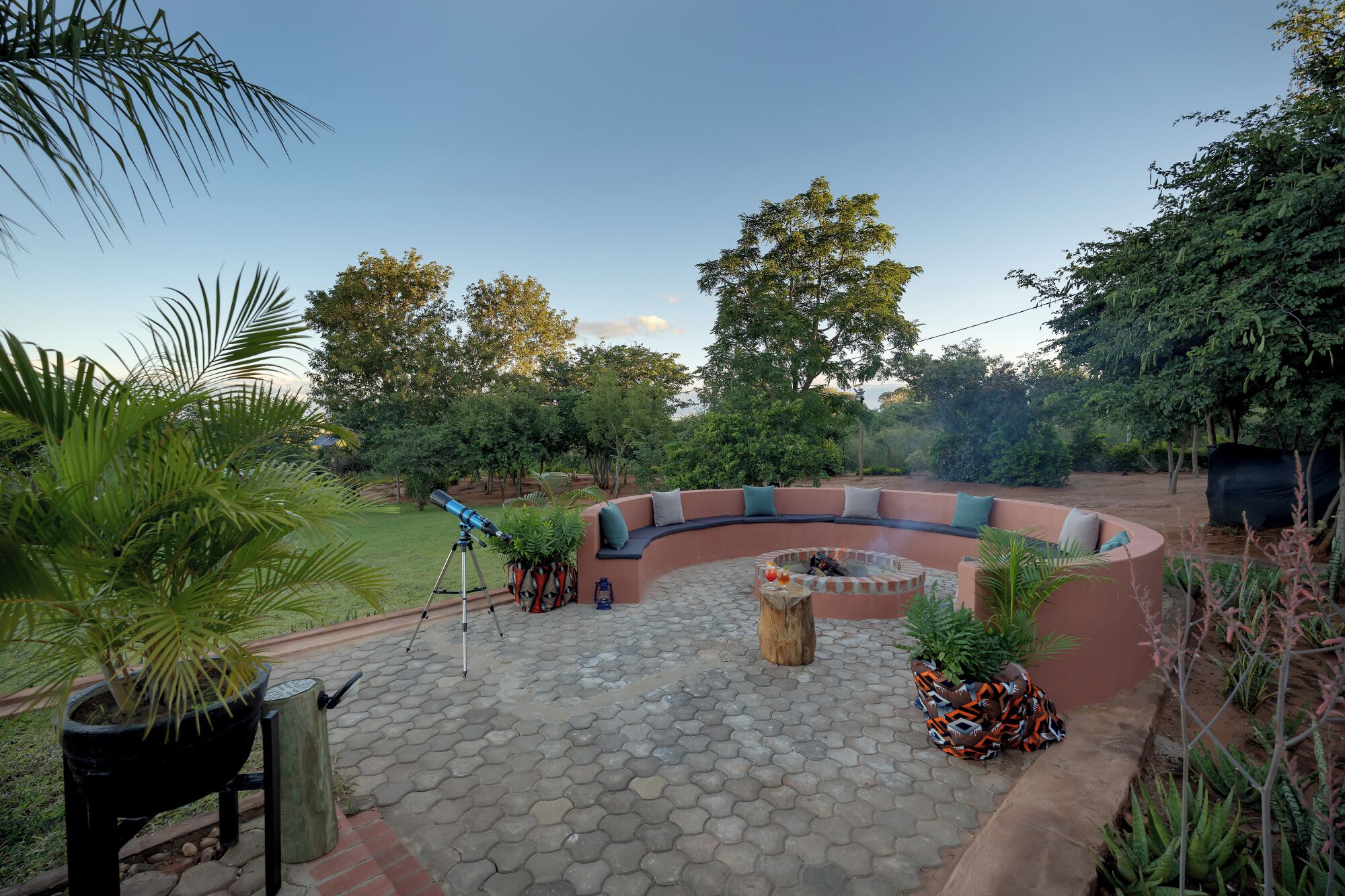 A curved outdoor seating area with a telescope, surrounded by lush greenery and trees.