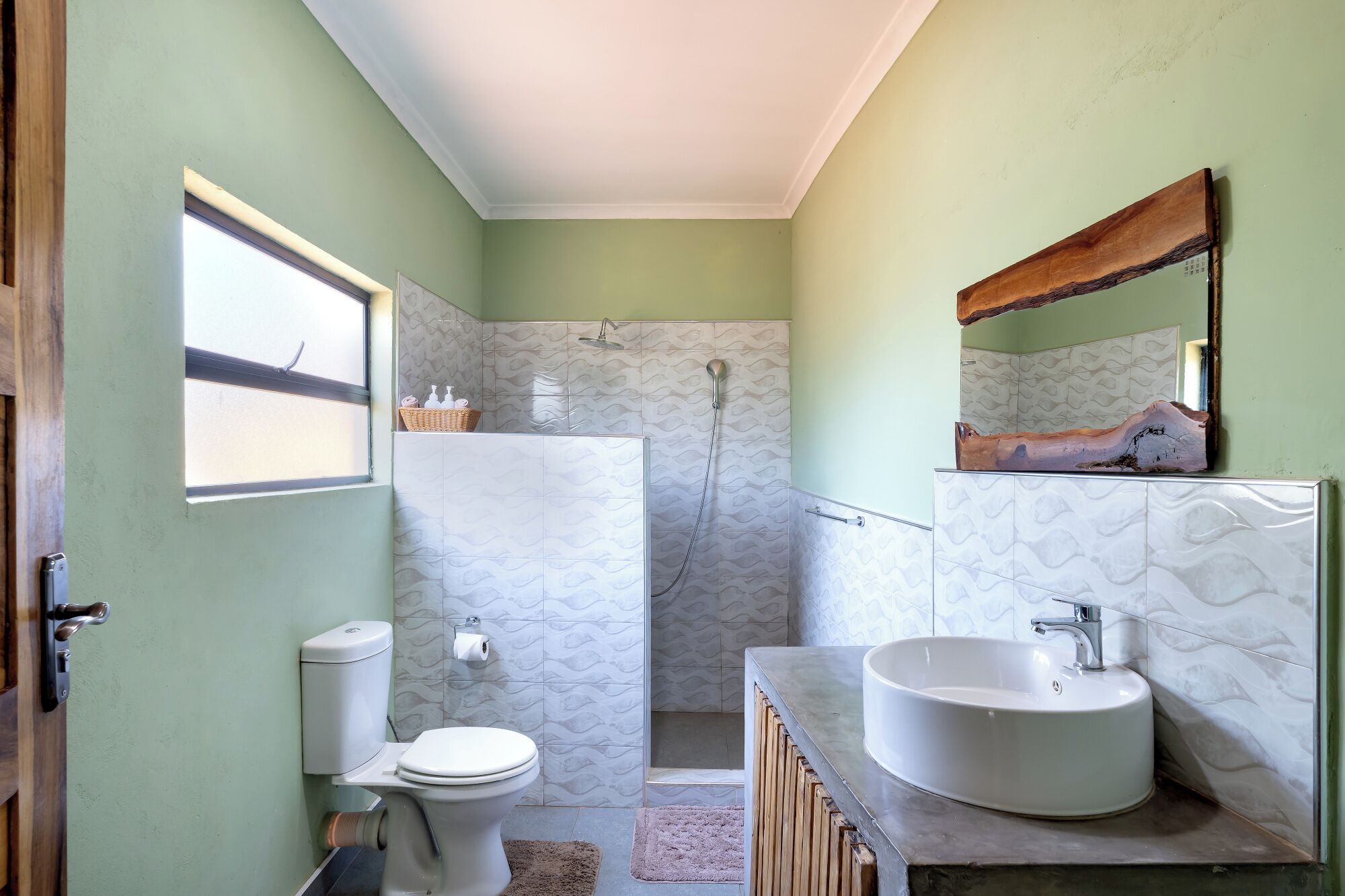 A bathroom with a toilet, shower, sink, and a mirror.