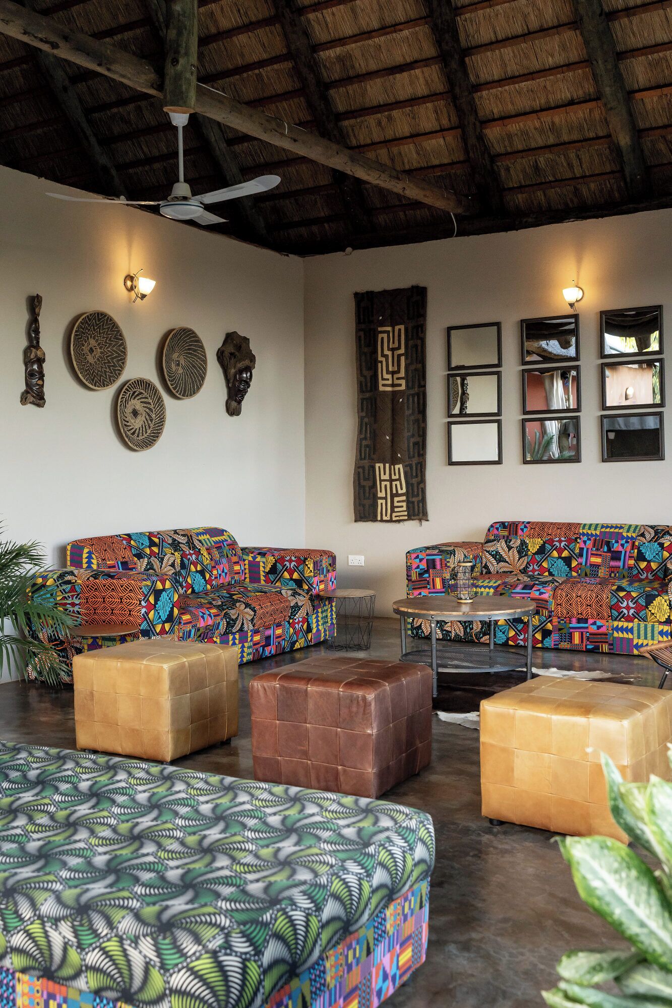A room with a high ceiling, a ceiling fan, patterned sofas, a coffee table, and wall decor.