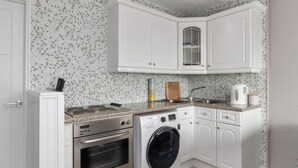 Cozinha compacta com armários brancos, forno embutido, máquina de lavar e micro-ondas.