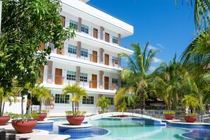 Un hôtel doté d’une piscine, entouré de palmiers et agrémenté de plantes en pot.