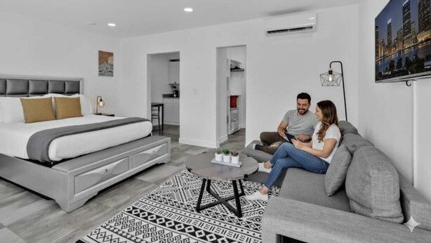 Un dormitorio moderno con una cama, un sofá gris, una mesa de centro y una alfombra estampada.