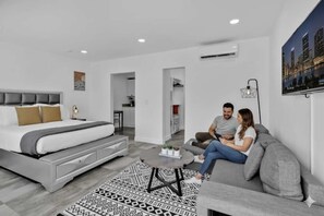 Une chambre à coucher moderne avec un lit, un canapé gris, une table basse et un tapis à motifs.