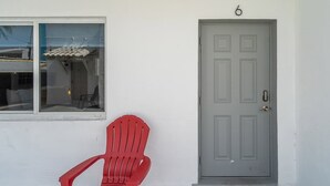 Una silla roja de plástico al aire libre, frente a un edificio con una puerta gris numerada con el número 6.