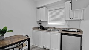 Una cocina compacta con armarios blancos, encimera de madera, un lavabo y lavavajillas.