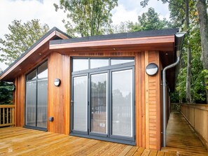 Une cabane moderne en bois, dotée de grandes portes-fenêtres coulissantes, d’une terrasse et d’un toit à forte pente.