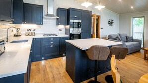Une cuisine moderne avec des meubles de couleur sombre, un îlot central et un coin repas équipé de deux tabourets de bar.