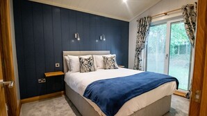 Une chambre avec un grand lit, des murs bleu foncé, une fenêtre avec des rideaux et un plancher en bois.