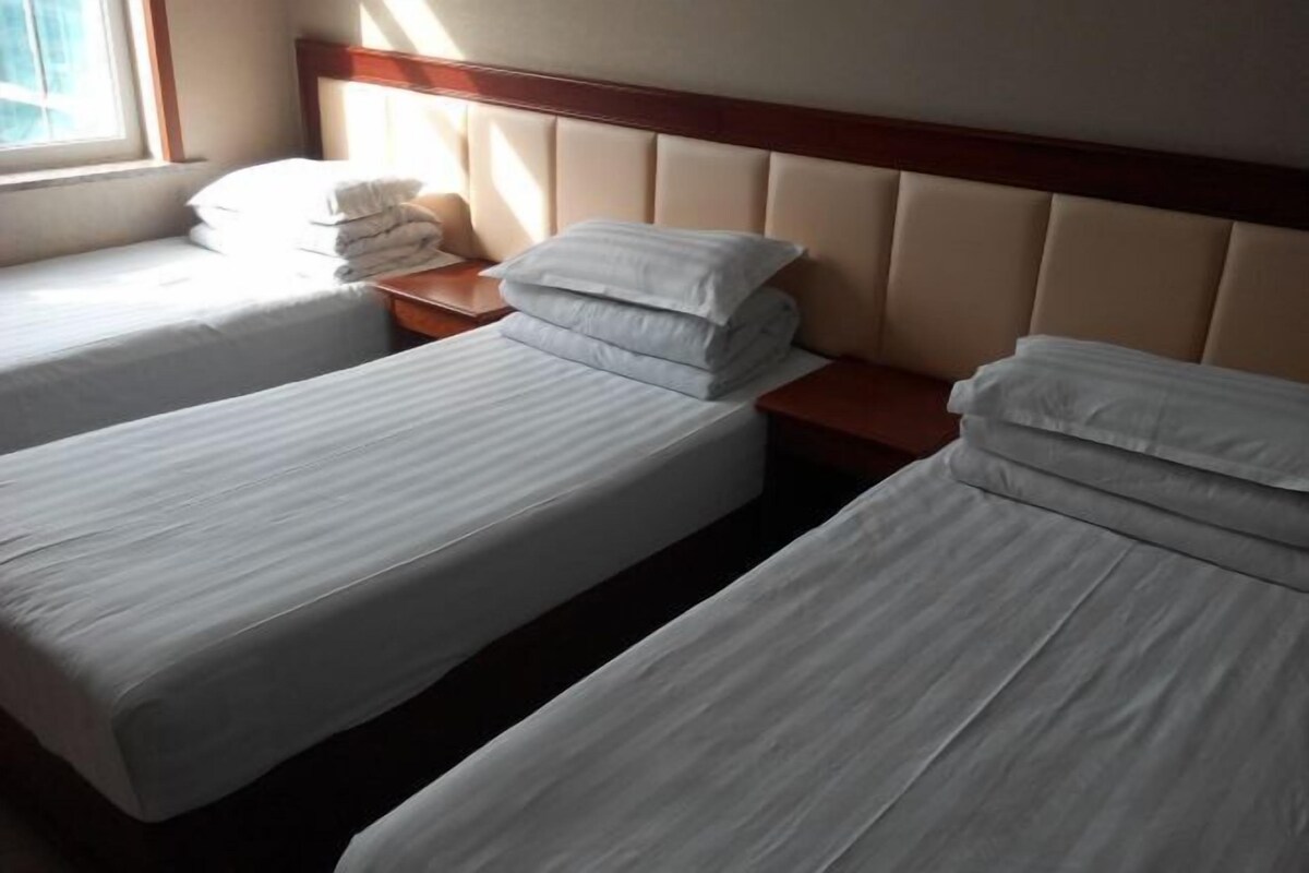 A hotel room with two single beds, a wooden headboard, and a window providing natural light.